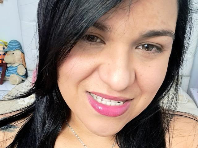 VivianaThompson has black hair, brown eyes, pink lipstick, and a slight smile. She's wearing a necklace and has a cute stuffed bear in the background.