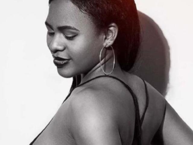 EbonySkyX a la peau foncée, les yeux fermés, et porte de grandes boucles d'oreilles. Elle regarde vers le bas, montrant son dos avec un haut sans bretelles. Ses fesses sont visibles. Noir et blanc..