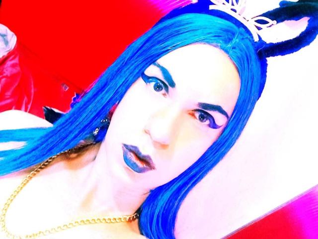 Bellanida, avec ses cheveux bleus, son eye-liner noir et son rouge à lèvres bleu, porte une chaîne en or et des oreilles de lapin noires. Elle a un visage blanc et un fond rouge. Ses lèvres sont légèrement entrouvertes..