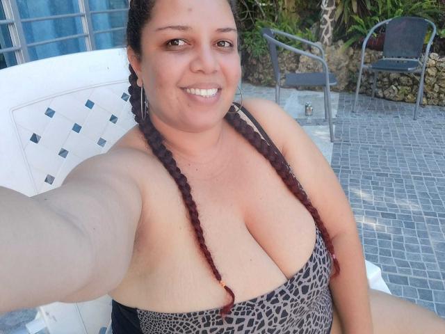 AdelineLox with large boobs, brown braided hair, smiling, wearing a leopard print bikini, sitting outside, taking a selfie, showing a relaxed, happy face.