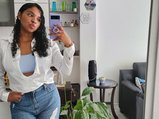 LisaMendez with curly black hair, white button-down shirt, blue crop top, and high-waisted ripped jeans, posing in mirror selfie, showing her tits and ass, holding purple phone.