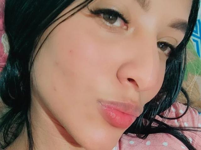 Het gezicht van VickyHoney, met zwart haar, lichte huid, bruine ogen en roze lippen, toont een lichte frons. Haar neus is klein en er is een kleine vlek op haar linkerwang..