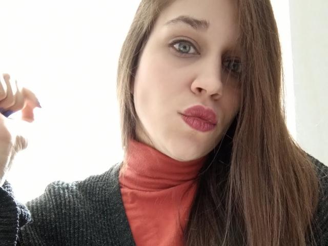 Faroles heeft lang bruin haar, een lichte huid, blauwe ogen en rode lippenstift. Ze draagt een rode coltrui en een donkergrijze trui. Haar rechterhand is iets omhoog..