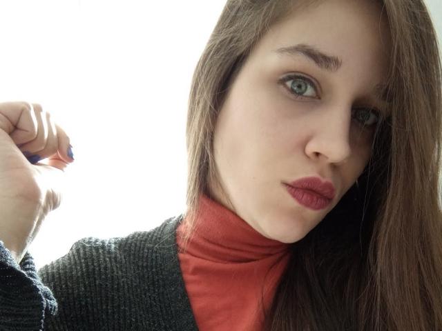 Faroles heeft een bleke huid, groene ogen en rode lippen. Ze draagt een grijze trui over een rode coltrui, met bruin haar dat naar de zijkant valt. Haar hand is omhoog..
