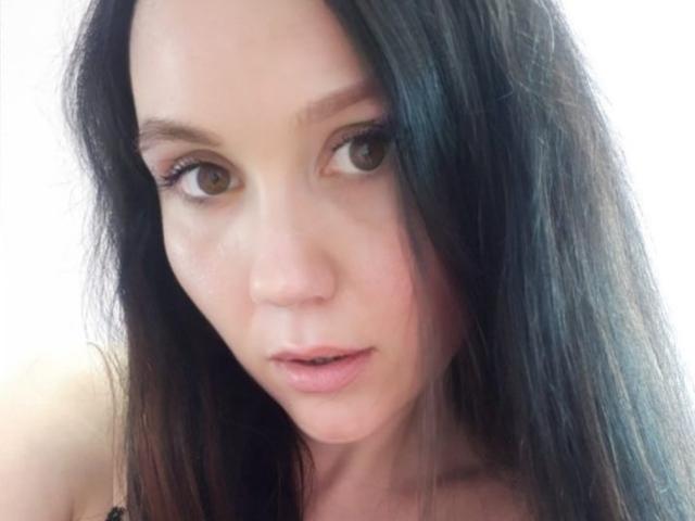 RittaSweetRose has long black hair, brown eyes, and slightly parted pink lips. Her face is centered with a soft, natural look and minimal makeup.