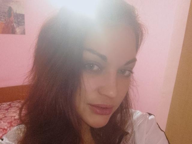 EvaAlferash has dark brown hair, light skin, and is looking at the camera with a slight smile. She has pink lipstick and is wearing a white shirt.