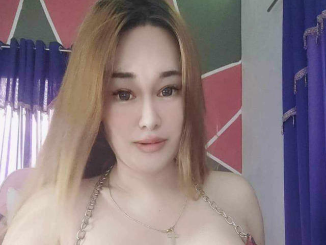 QuuenBeeTs tiene el cabello castaño claro, piel clara y ojos marrones, lleva un collar de cadena y muestra sus pechos pequeños a medianos en un selfie..