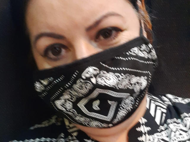 LolaGreate has dark eyes, thick eyebrows, and is wearing a black and white patterned mask covering her lower face. She's looking up with a slightly tilted head.