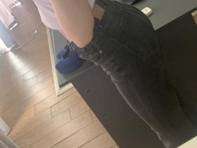 Los jeans de mezclilla negros y de cintura alta de Tserera, que muestran sus curvas en los glúteos y la cintura, con un cinturón marrón visible. Lleva una camiseta blanca, acanalada y de manga corta..