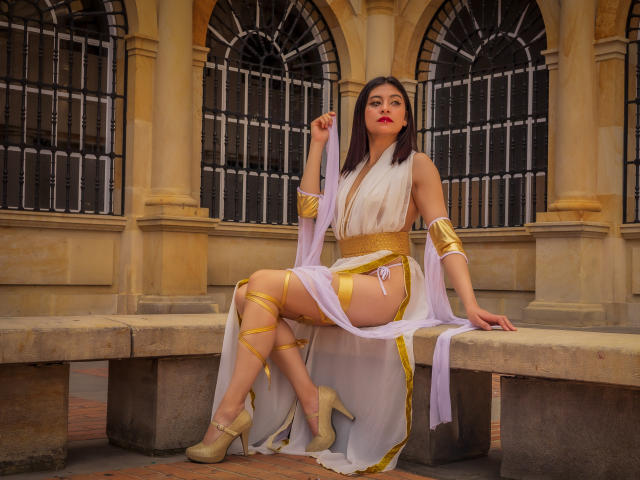 SamanthaSmith, in a Greek-style outfit, sits on a stone bench with a white and gold dress, showing her tits, ass, and thighs, wearing high heels, holding a dress piece.
