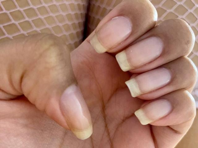 La main de JessicaSoler, avec des ongles à pointe française, mettant en valeur ses ongles propres, d'un rose pâle, et ses doigts légèrement courbés, avec le petit doigt légèrement relevé. Elle porte un collant de pêche sur son bras..