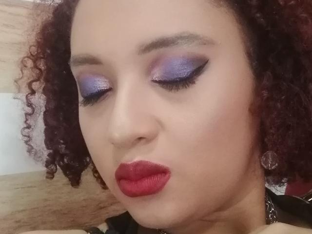 VioletaSwitch's face, with purple eyeshadow, red lipstick, and curly red-brown hair, eyes closed, wearing black necklace, looking cute and sexy. Boobs not visible, focus on face.