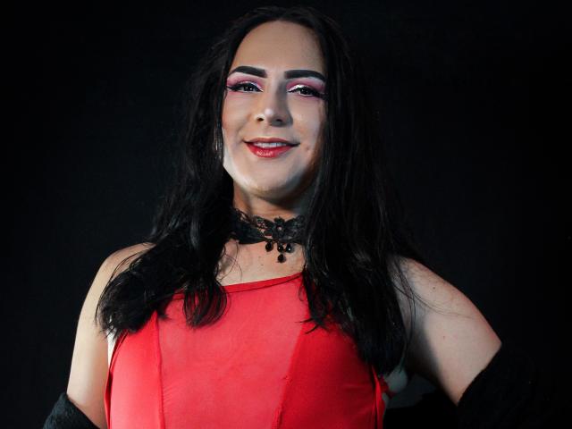 IrisDurand with long black hair, red dress, black lace choker, pink and purple eye makeup, smiling, red lipstick, black background, medium breast size, soft light, confident.