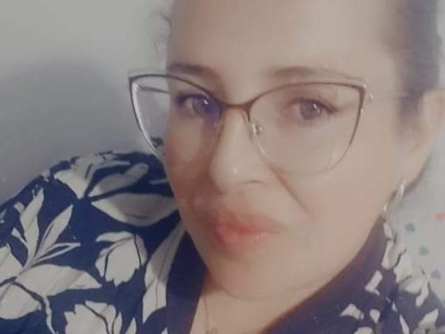 CandHoney with glasses, puffy lips, and a patterned shirt, looking slightly up. Her face is partially blurred, with a light skin tone and dark hair.
