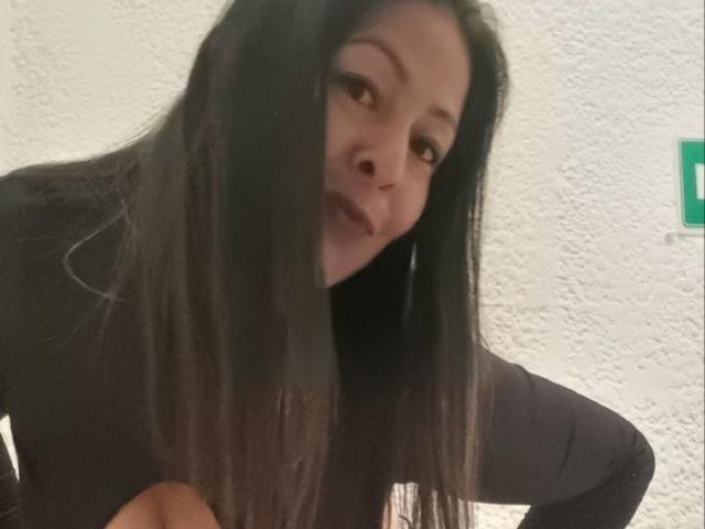 CatalinaJH tem cabelos pretos longos, olhos castanhos e um sorriso discreto. Ela está vestindo uma gola alta preta, e suas mãos estão perto do rosto. Suas nádegas não estão visíveis..