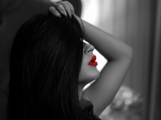 I capelli neri di EveMusette, le labbra rosse e il braccio sollevato in una fotografia in bianco e nero, con la mano tra i capelli, che mette in risalto il suo bel rossetto rosso e la sua pelle liscia..