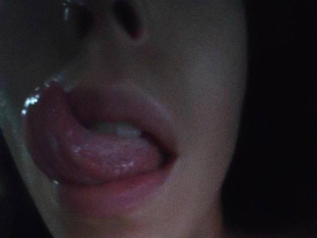 SeleneBright's glossy, pink-tinged tongue is partially out, wet, and resting on her upper lip, with her moist, slightly parted lips visible. The focus is on her face.
