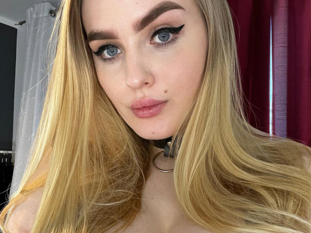 OliviaBent a les cheveux blonds, les yeux bleus, un eye-liner noir, des lèvres roses, une petite tache de beauté sur sa joue droite, et un collier noir avec un anneau. Ses seins sont légèrement visibles..