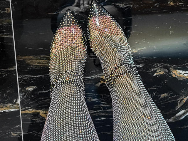 GoddessKaterina's legs in sparkly, studded, metallic high heels with pointed toes, standing on a shiny black marble floor. Her feet are the focal point.