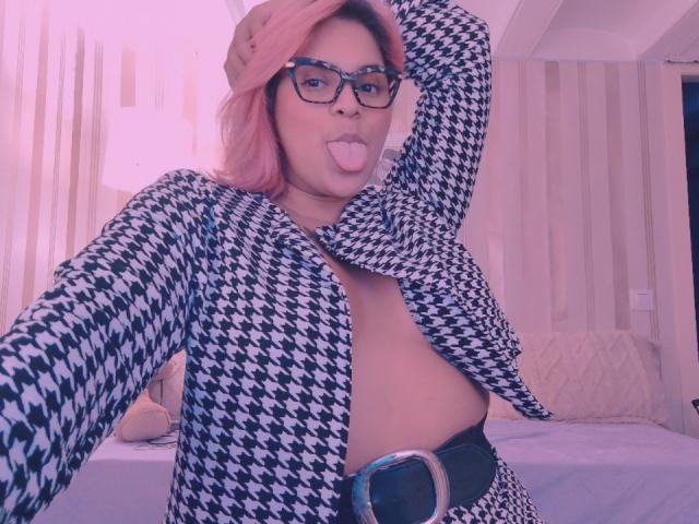 Chili with pink hair and glasses is sticking out her tongue, wearing an open houndstooth top exposing one large breast.