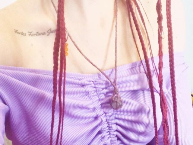 Zanoza's tits are covered in a purple off-shoulder top with red braids hanging down, wearing a necklace with a small rock.