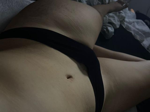VanellopeWow's blote buik met een kleine navel, draagt zwarte onderbroek, ligt plat met benen lichtjes gespreid, met zichtbare stretchmarks en lichte huid..