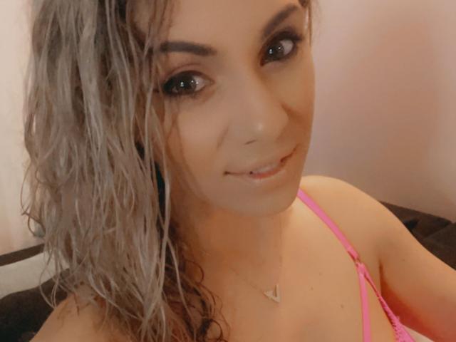 LucilleXSugar ha i capelli grigi, ricci e umidi, gli occhi marroni e un leggero sorriso. Indossa un reggiseno rosa e una collana con un ciondolo a forma di cuore. Il suo seno è visibile..