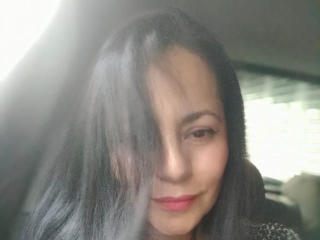 EkaterinaSex hat schwarzes Haar, das ein Auge bedeckt, hellbraune Haut und pinken Lippenstift. Sie lächelt sanft in einem Auto, durch das Sonnenlicht scheint. Ihr Hintern ist nicht sichtbar..