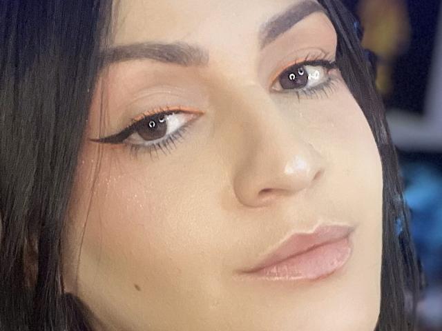 ElinaJhonson's face with brown eyes, black eyeliner wings, and pinkish lips. She has dark, straight hair, light skin, and a small beauty mark near her left cheek.