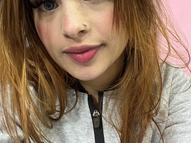 ShantalSummer has a nose ring, pink lips, and long brown hair in a grey zip-up hoodie. Her blue eyes and slight smile are visible. She's looking at the camera.
