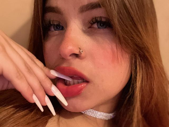 ShantalSummer's face, with pink lips and long white nails, is holding a white toothbrush near her slightly open mouth, showing a nose piercing and wearing a sparkling choker.