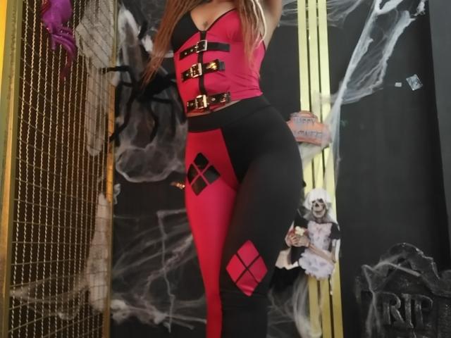 KendallQuinn wearing a red and black strapless top with gold buckles and matching high-waisted black and red leggings, showing her ass and a diamond pattern on her thighs.