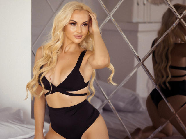 Blonde Klubnika with long wavy hair, black strappy bikini, showing her tits and ass, hand in hair, mirror reflection, white bedroom, soft lighting, sexy, confident, full-figured.