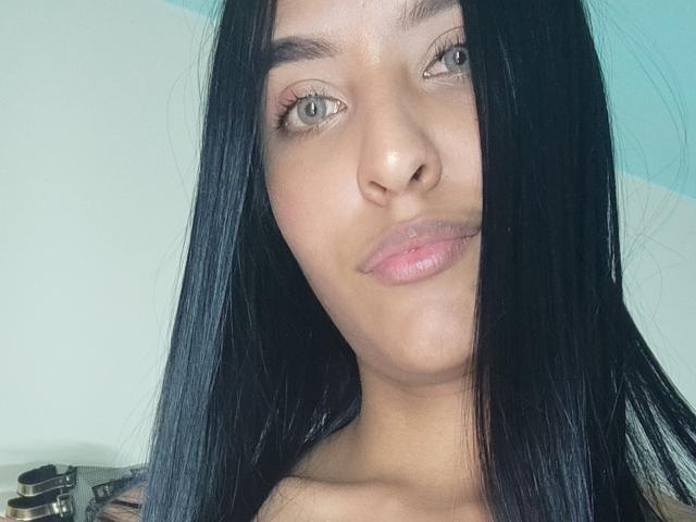 VickyHoney ha i capelli neri e lisci, gli occhi verdi e le labbra rosate. La sua pelle è abbronzata e sta facendo una smorfia. Il suo seno non è visibile..