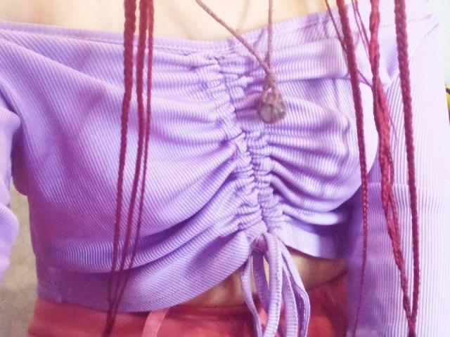 La maglia viola a coste di Zanoza, con spalline scoperte e un nodo, che lascia intravedere un po' il seno, ha dei capelli intrecciati rossi davanti e una collana di pietre..