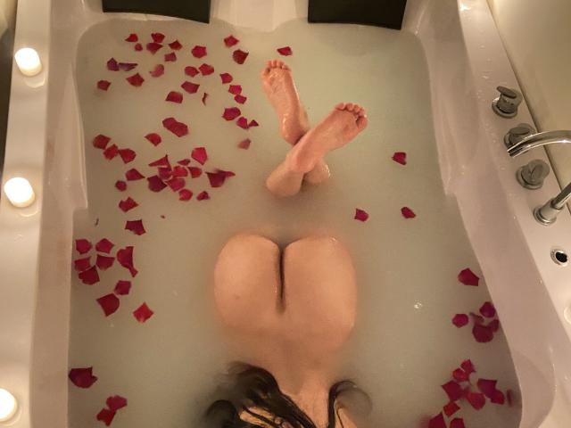 Les fesses de Tina et Edward sont dans une baignoire blanche remplie d'eau et de pétales de roses rouges. Ses jambes sont croisées aux chevilles, et des bougies sont allumées autour de la baignoire..
