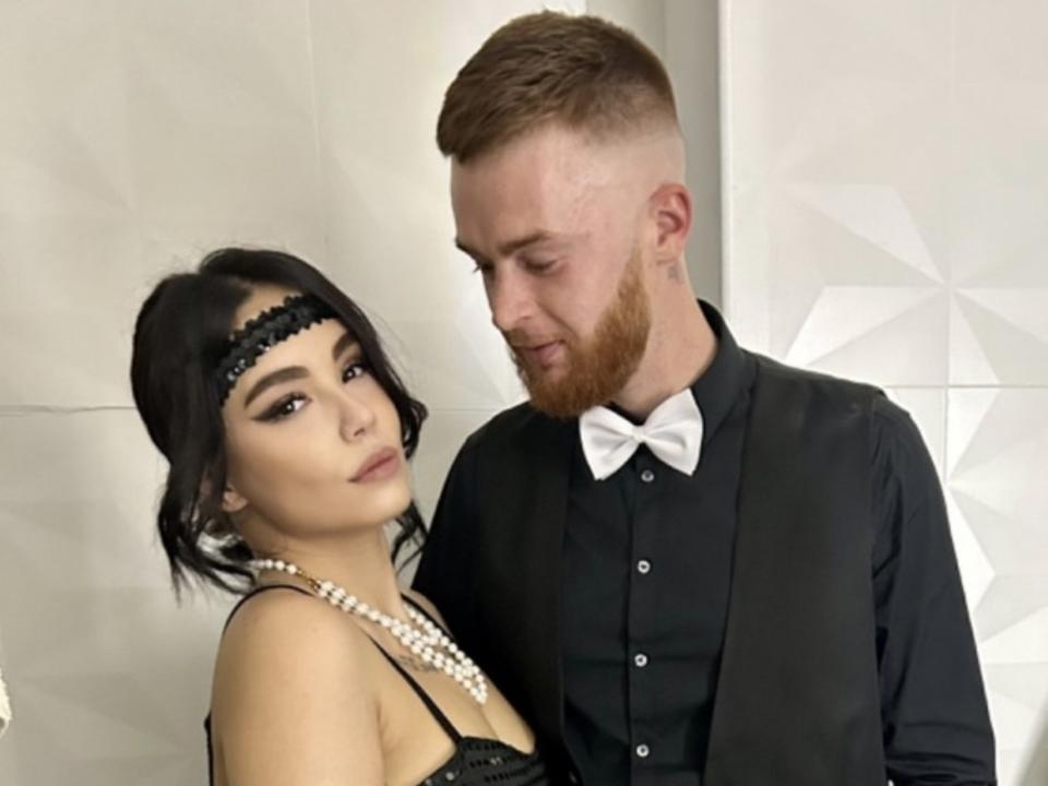 Kassi heeft zwart haar, een zwarte kanten hoofdband en een parelketting, en draagt een zwarte jurk. Billy heeft een rode baard, een witte vlinderdas en een zwart pak, en kijkt naar beneden..