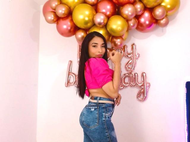 SarahyJhones, con cabello largo y oscuro, blusa rosa, jeans azules, de pie, mirando por encima del hombro, sosteniendo un globo, globos rosas y dorados, mostrando su trasero, linda, sexy, en interiores..
