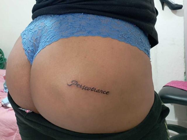 As calcinhas azuis de renda de LiAngel estão puxadas para baixo, revelando seu bumbum, com uma tatuagem que diz "Prestance" em sua bochecha esquerda. Sua camisa preta está parcialmente visível..