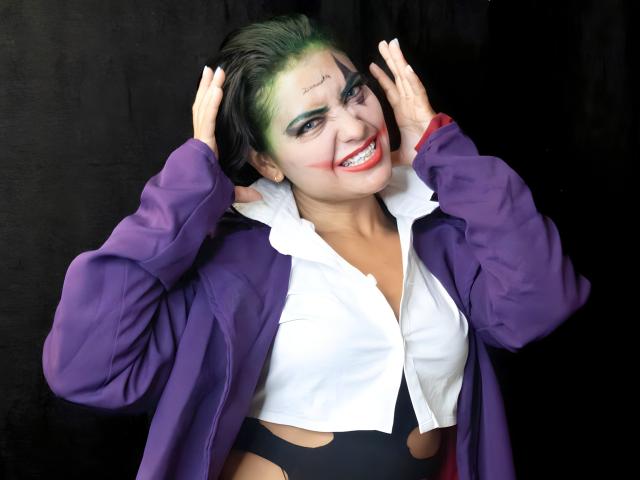 Silvanna Reyes mit grün gefärbtem Haar, weißem Hemd, schwarzer Hose mit Ausschnitten, lila Jacke, lächelnd, Hände im Haar, roter Lippenstift, schwarzer Hintergrund, sieht glücklich aus, Brüste sichtbar, süß, Cosplay..