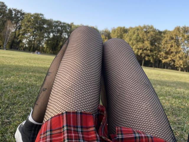 Les jambes de Zuckerberg, portant des bas en filet et une jupe à carreaux rouges, les genoux serrés, vue de derrière, chaussées de baskets noires et blanches, sur de l'herbe..