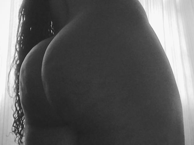 Il grande sedere di AmandaLick è in primo piano, scuro e con una texture particolare, con lunghi capelli ricci sul lato sinistro, in una fotografia in bianco e nero..
