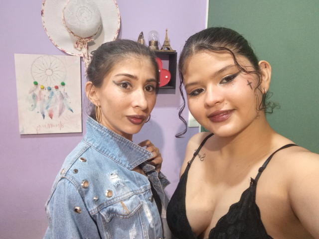 Angela e Barbara, due donne con la pelle media e i capelli scuri, indossano una giacca di jeans e una maglia nera in pizzo, che mostrano il seno, in piedi una accanto all'altra, sorridendo alla fotocamera..