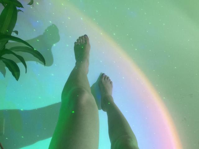 De benen, voeten en tenen van KatherinGrey zijn in de lucht, met een lichtgroene regenboog en glinsterende sterren op de achtergrond. Haar tenen zijn lichtelijk vuil, en er staat een plant aan de linkerkant..