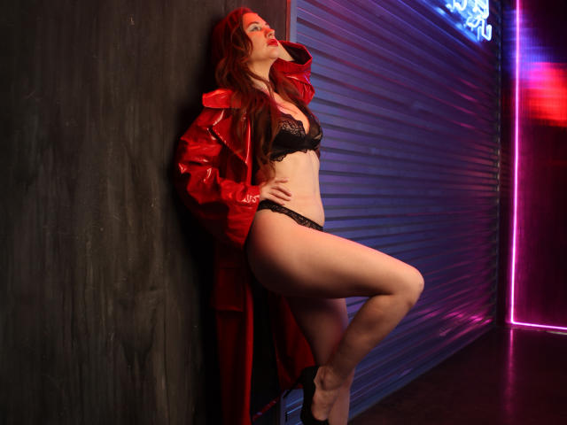 DashaHart with red coat, black lace bra, and panties, leaning against wall, red hair, red lips, hand on hip, neon lights, curvy, sexy, pale skin, leg raised.