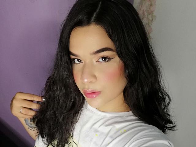 Antonela, con cabello negro ondulado, rubor rosado y delineador de ojos alado, vestida con una camiseta blanca, mirando a la cámara con un labio ligeramente entreabierto y de color rosa..