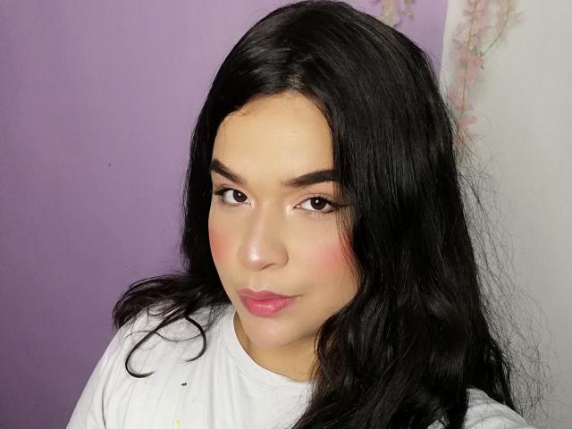 Antonela tiene el pelo largo y negro, ojos marrones, un rubor rosado en las mejillas y lápiz labial rosa. Lleva una camisa blanca, mirando ligeramente hacia un lado con una sonrisa sutil..