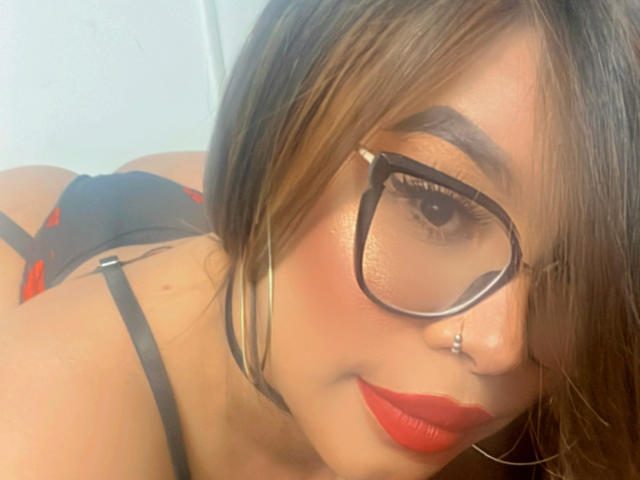 ValeriHarris ha gli occhiali, il rossetto rosso e un piercing al naso. Indossa della lingerie nera con dettagli rossi, e i suoi capelli castani coprono parzialmente il viso..