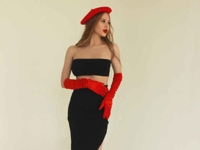 ViolettaSteward has red hat, red gloves, black strapless top, black skirt, and red lipstick, standing with hands on hip, showing her ass and tits in a photo.
