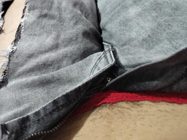 LuluFrancaise's blue denim shorts are partially unzipped, revealing red lace underwear and a hint of her hairy, tan-skinned pussy. The frayed edge adds a rough, casual look.